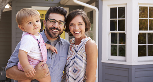 Home Insurannce: Young couple with a toddler standing in-front of their new home